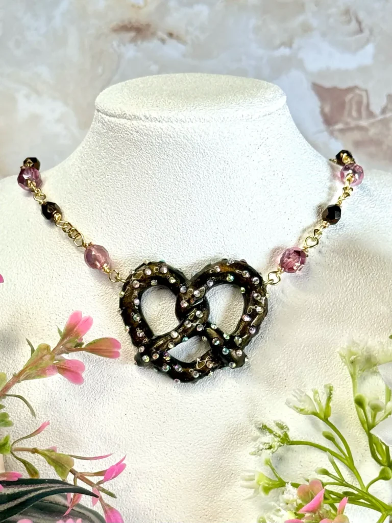 bronze pretzel pendant with rhinestones on a gold beaded chain featuring candy pink and bronze Preciosa beads. Designer Extender chain with three charms, star, bead and heart.