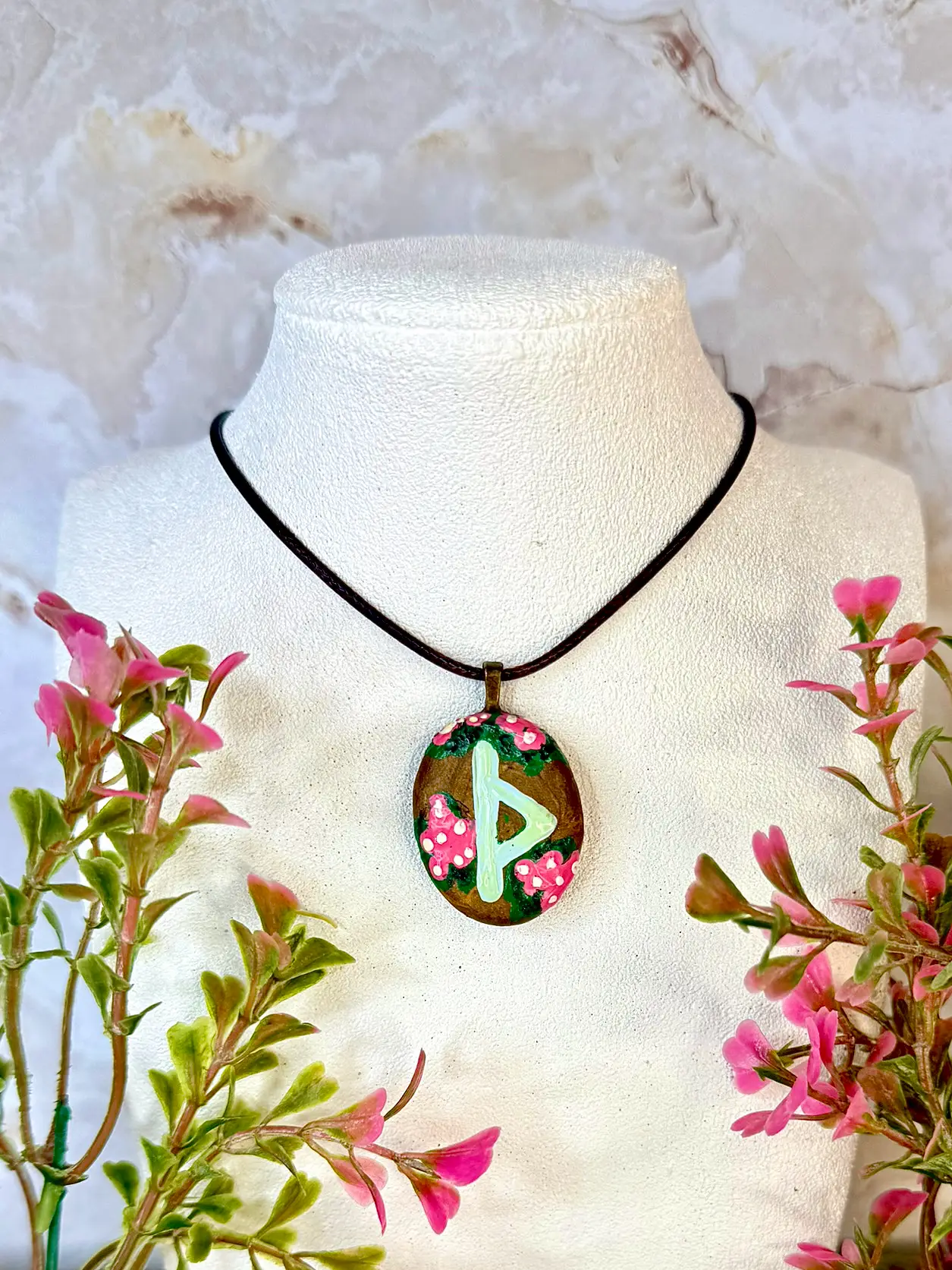 The Thurizaz Rune symbol painted in a luminous pale green onto an antique gold polymer clay oval cabochon, along with pink flowers. Quirky, elegant, and feminine.